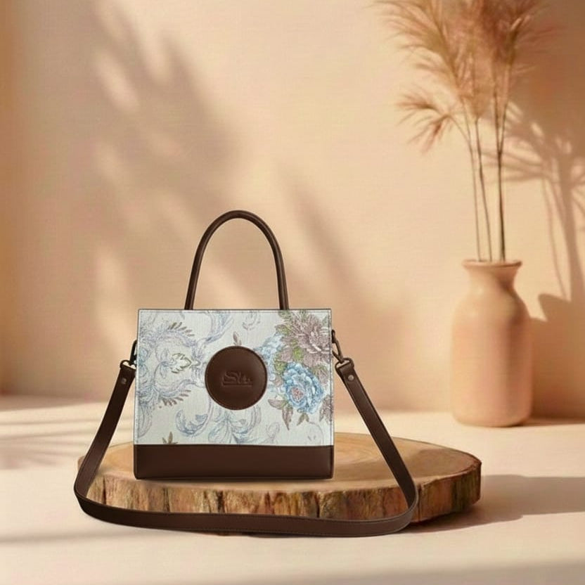 brown Handbag with floral design on a wooden stand against a beige wall with a vase of dried plants.