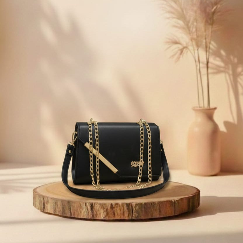 Black handbag with gold chain on a wooden platform against a beige background