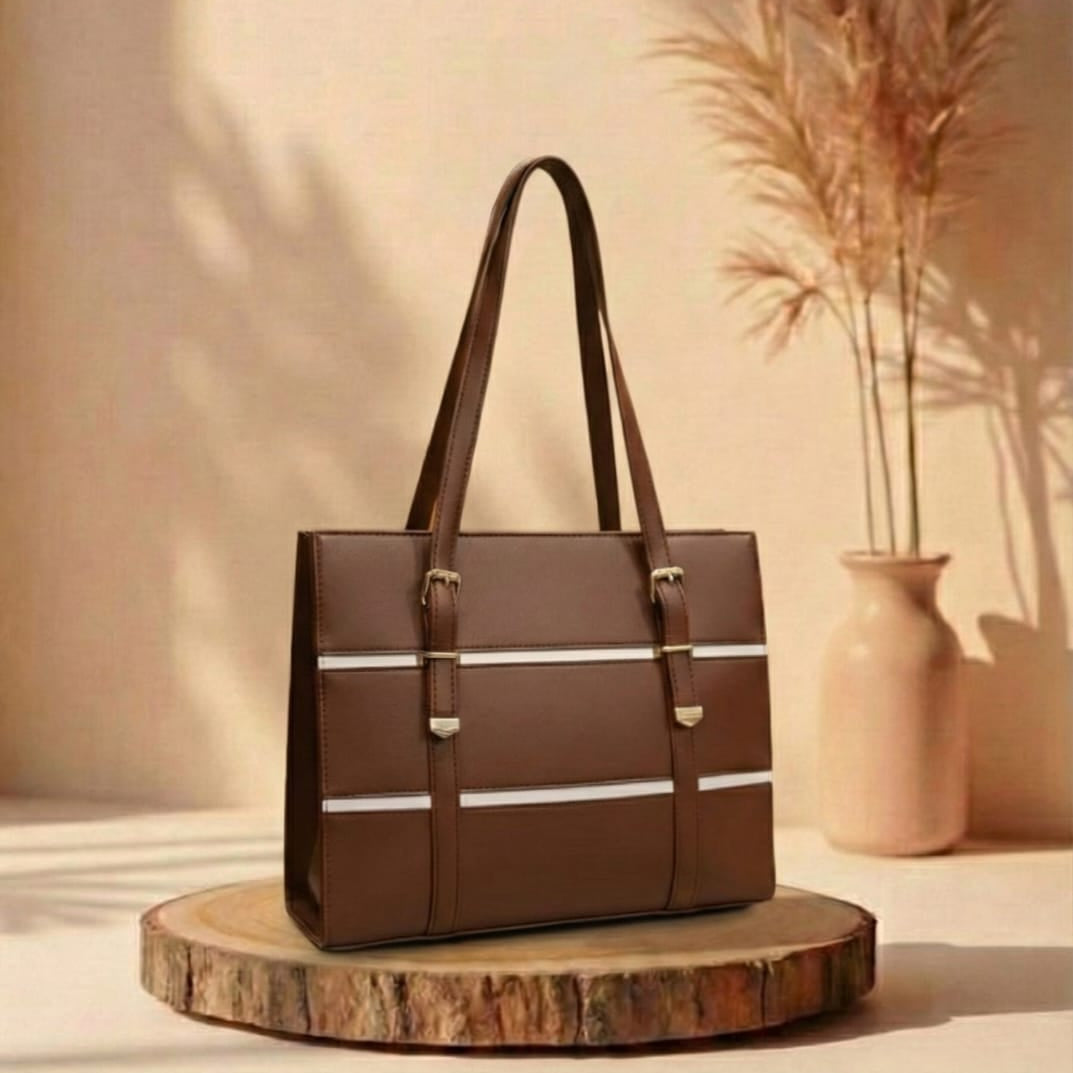 choco Brown handbag with white stripes on a wooden stand against a beige wall with a vase and plants.