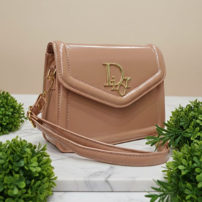Beige handbag with a brand logo on a marble surface with green plants.