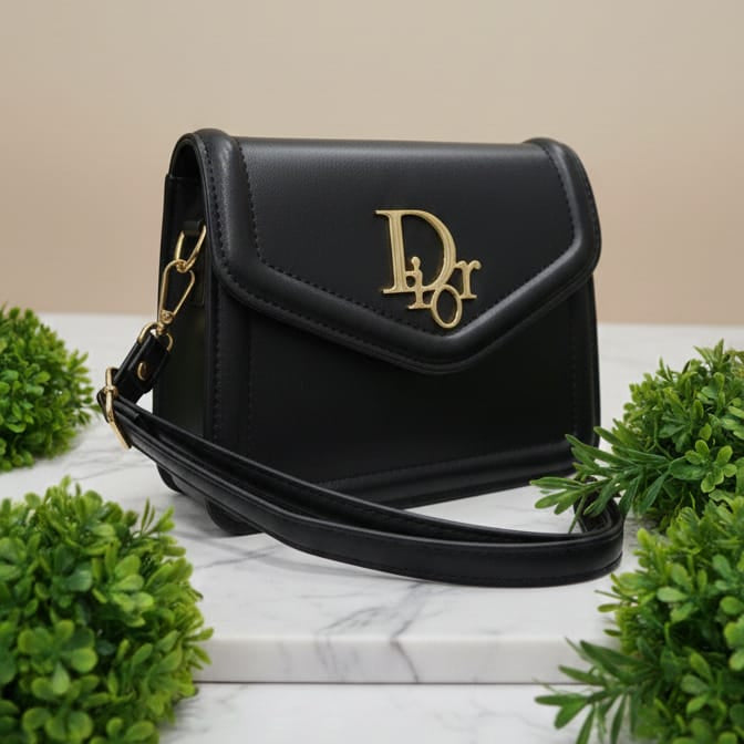 Black handbag with gold accents on a marble surface with greenery