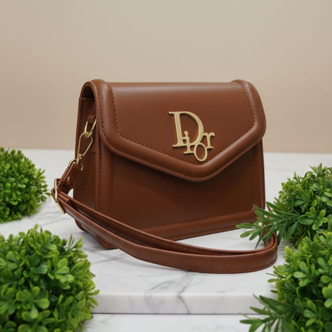Brown handbag with a visible brand logo on a marble surface with green plants.