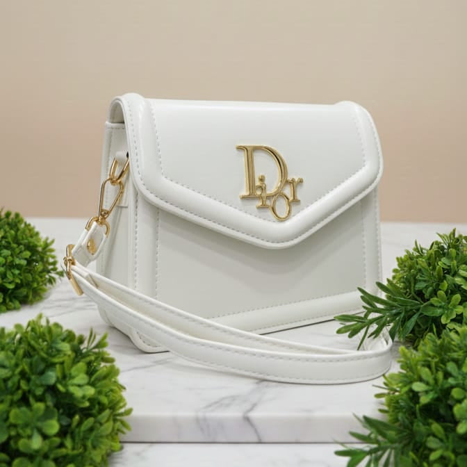 White handbag with gold logo on a marble surface with greenery