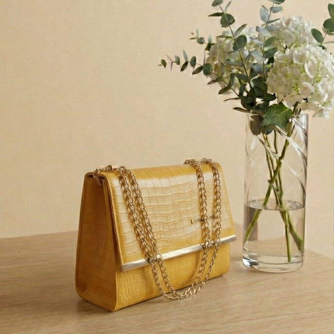 Yellow handbag on a wooden surface with a vase of flowers in the background